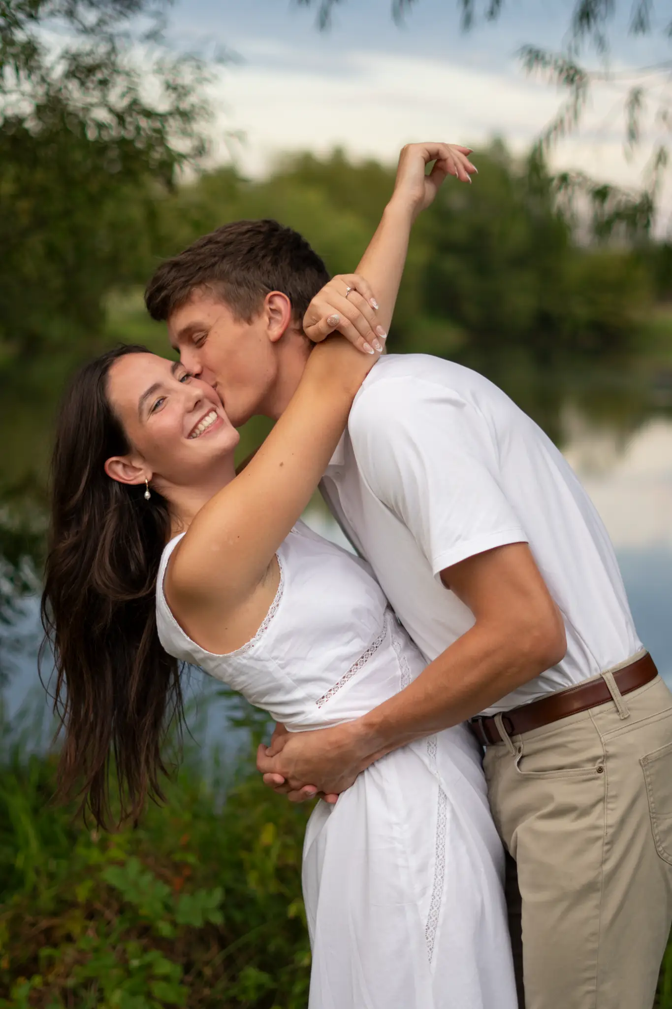 Nathan kissing Isabella’s cheek on the bank of a lake