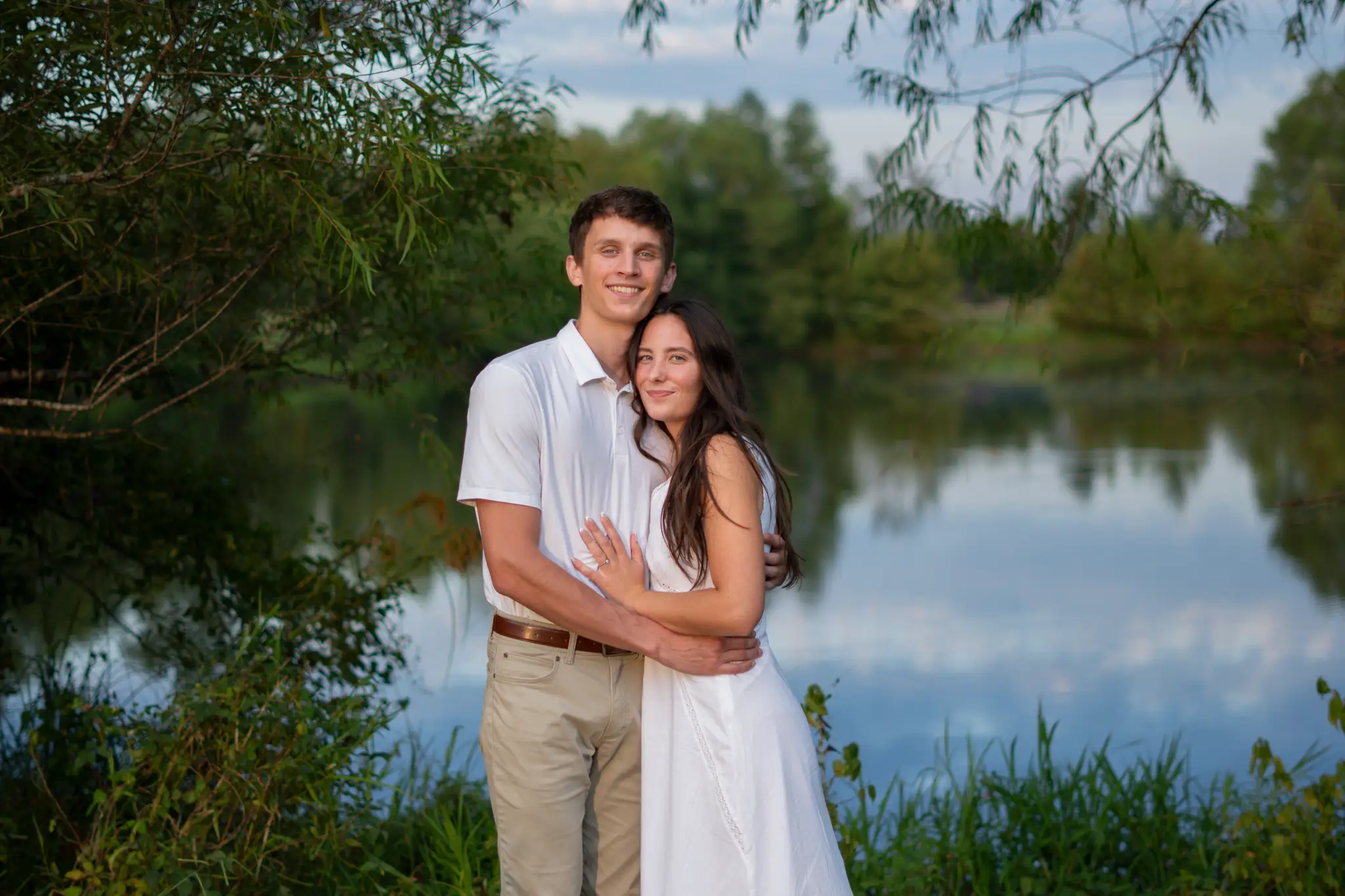 The couple in a quiet embrace beside still water at golden hour