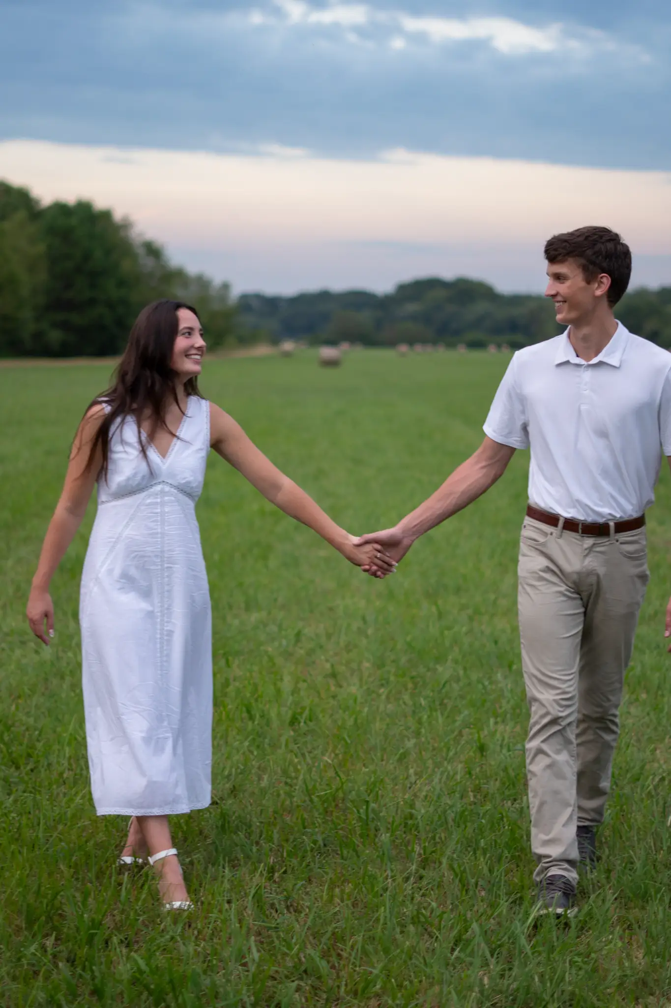 The two of them walking hand in hand across an open hayfield at sunset