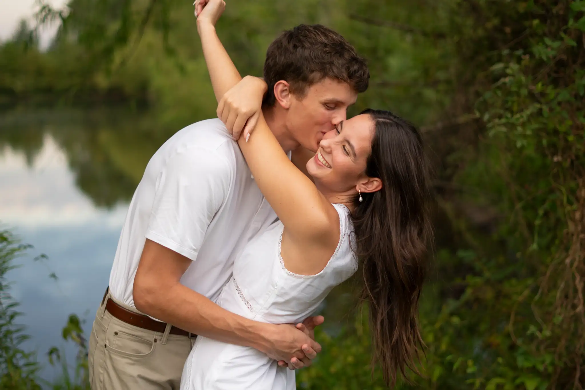 Isabella and Nathan laughing together beside a still lake at golden hour